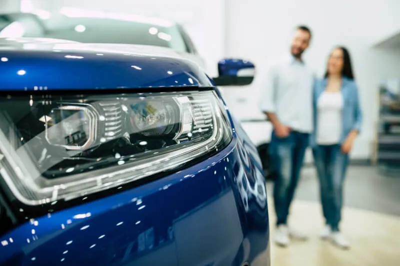 Macchina blu in primo piano con una coppia di ragazzi sullo sfondo