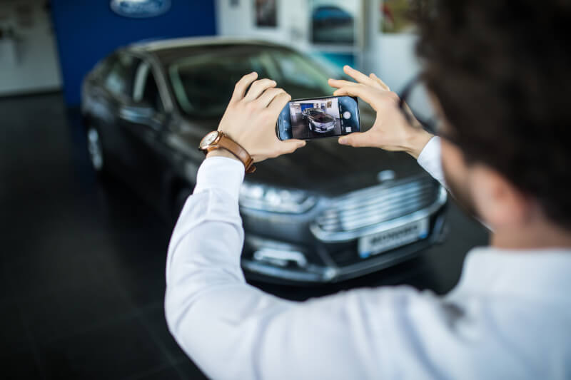 Uomo che scatta una fotografia ad una automobile con il cellulare